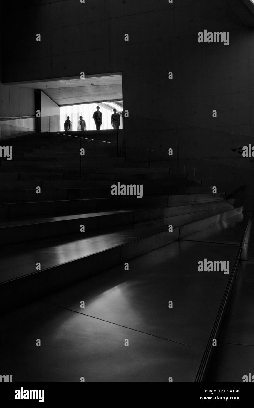 Strong silhouettes coming from the light into a dark stairs Stock Photo