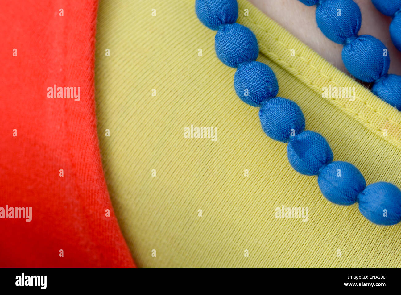 Blue beaded type necklace worn with yellow top and red cardigan Stock Photo