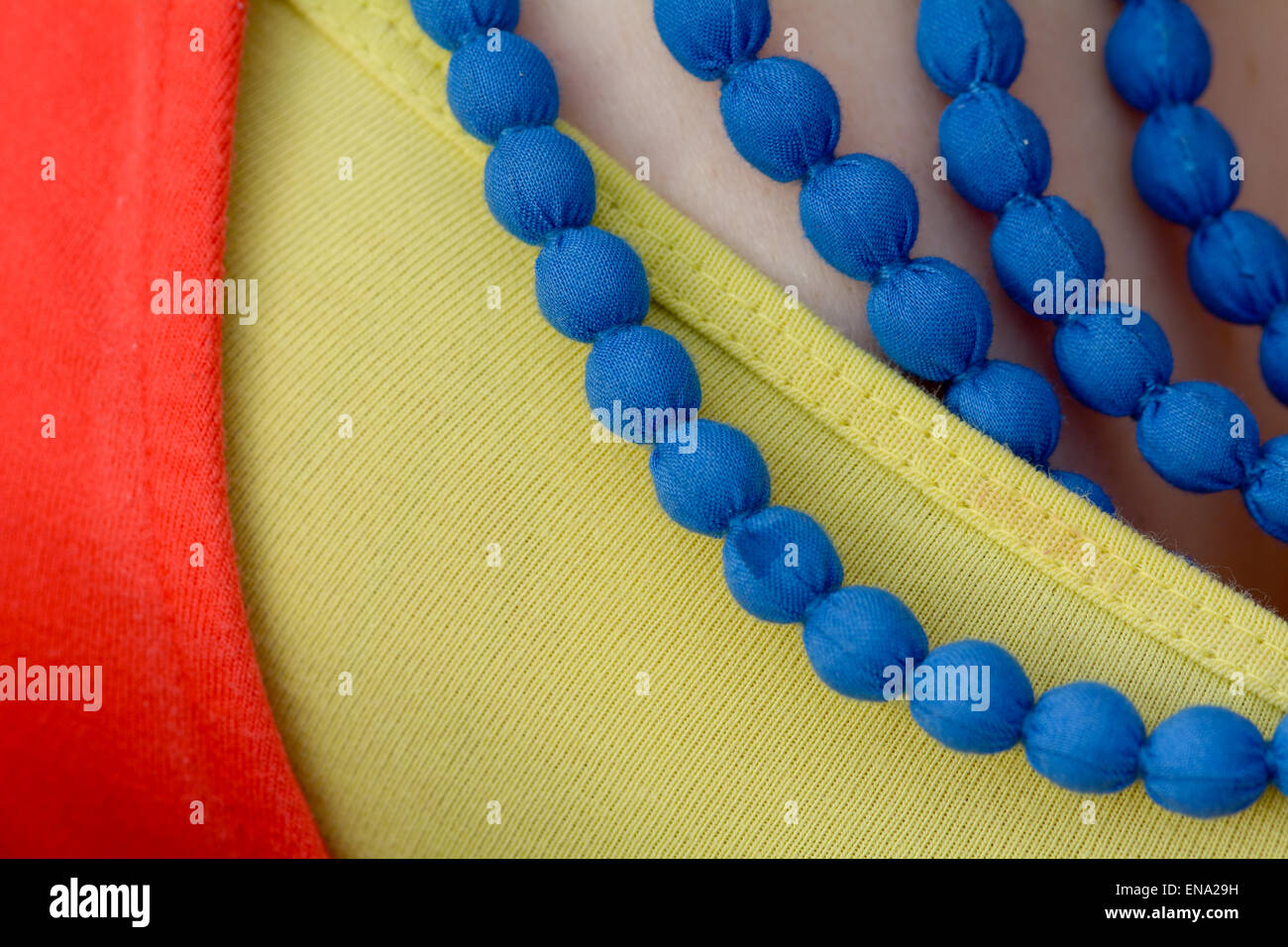 Blue beaded type necklace worn with yellow top and red cardigan Stock Photo