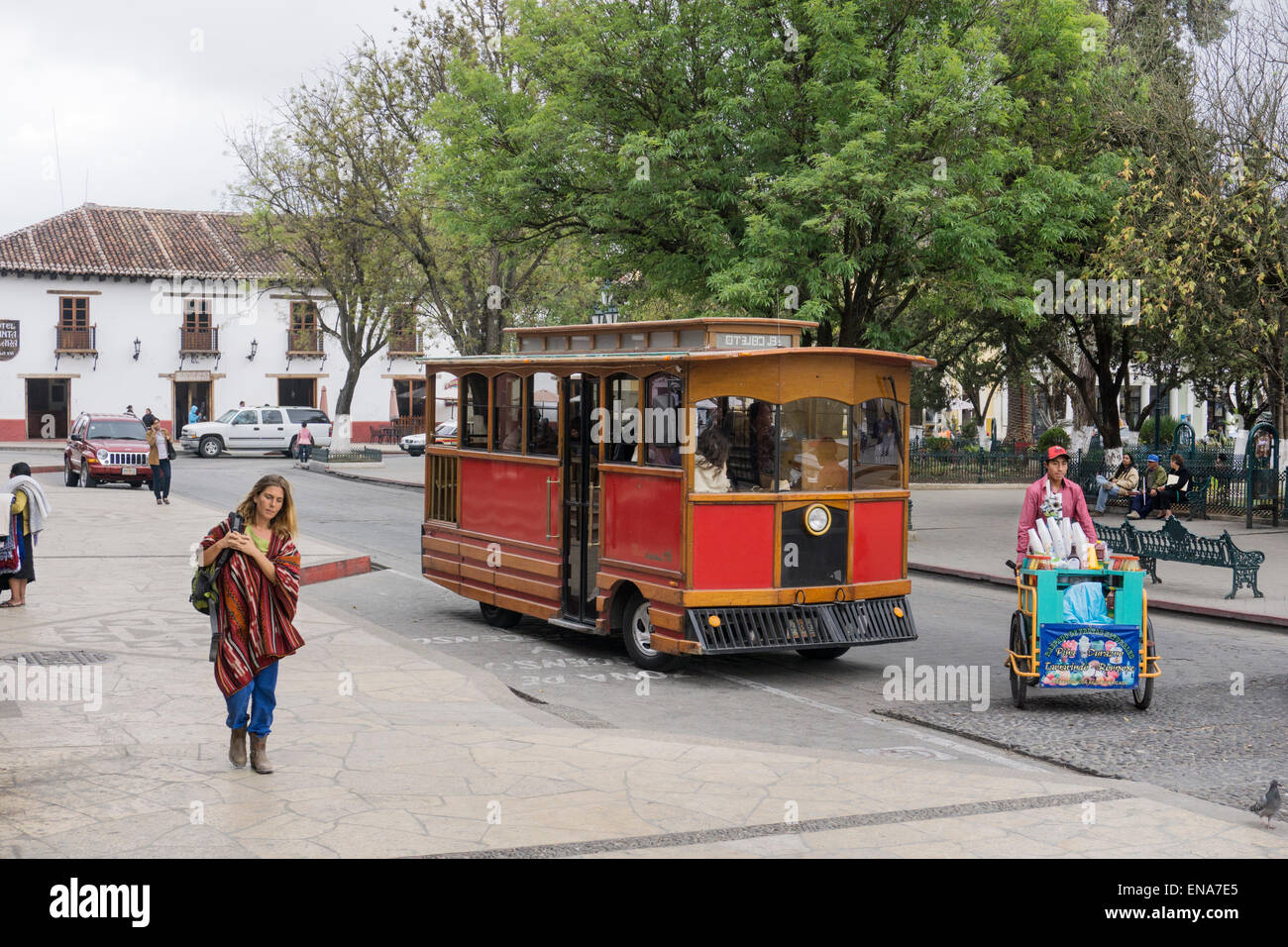 bright red sightseeing trolley doing tour of San Cristobal stops at Zocalo behind vendor with cart of refreshments refescas Stock Photo