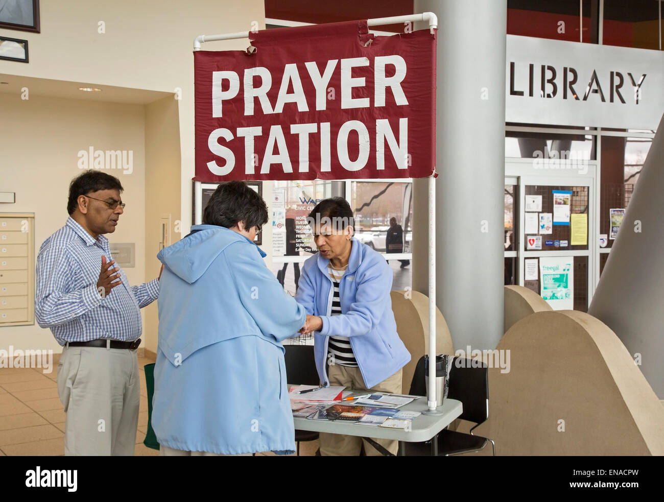 Warren, Michigan USA - Christian activists pray with a woman at their 'prayer station' in the lobby of city hall. A few steps away, atheists staff a 'reason station.' Originally, the city allowed only the prayer station. It took a federal court's order to allow the atheists to set up their table. Credit:  Jim West/Alamy Live News Stock Photo
