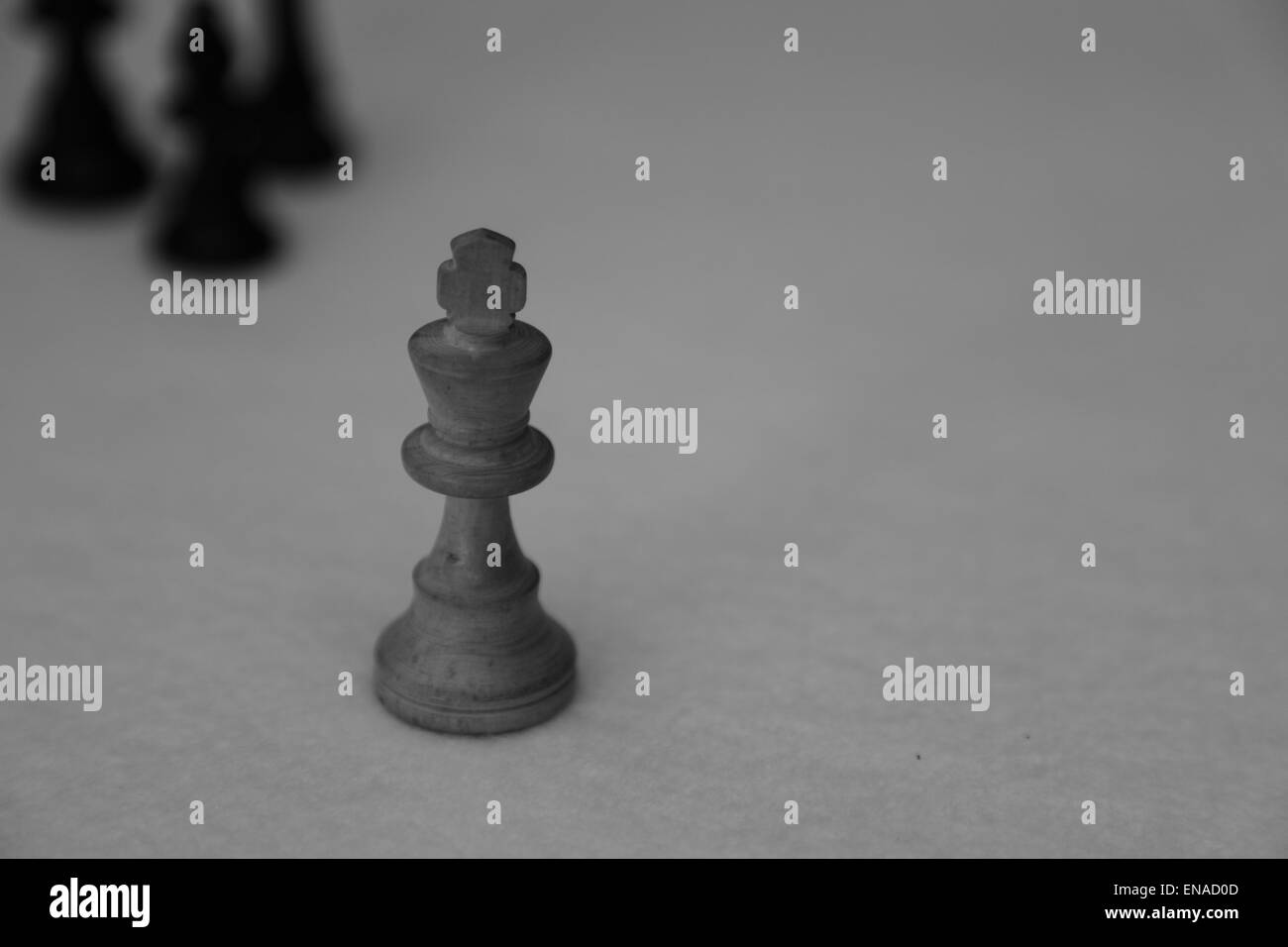 The white king from a chess set being menaced by three black chess pieces Stock Photo