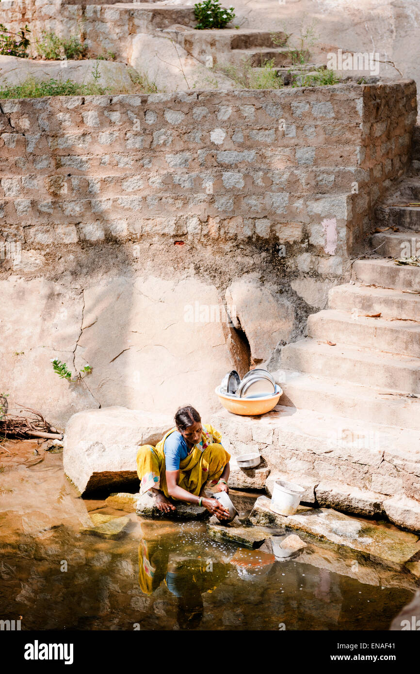 A woman washing the dishes in a stream, Anegundi. Stock Photo