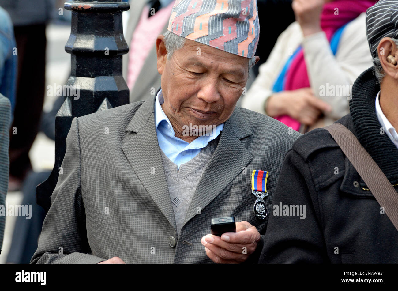 Elderly Nepalese man / retired Gurkha using his mobile phone, London 2015, wearing a Dhaka topi - traditional hat Stock Photo