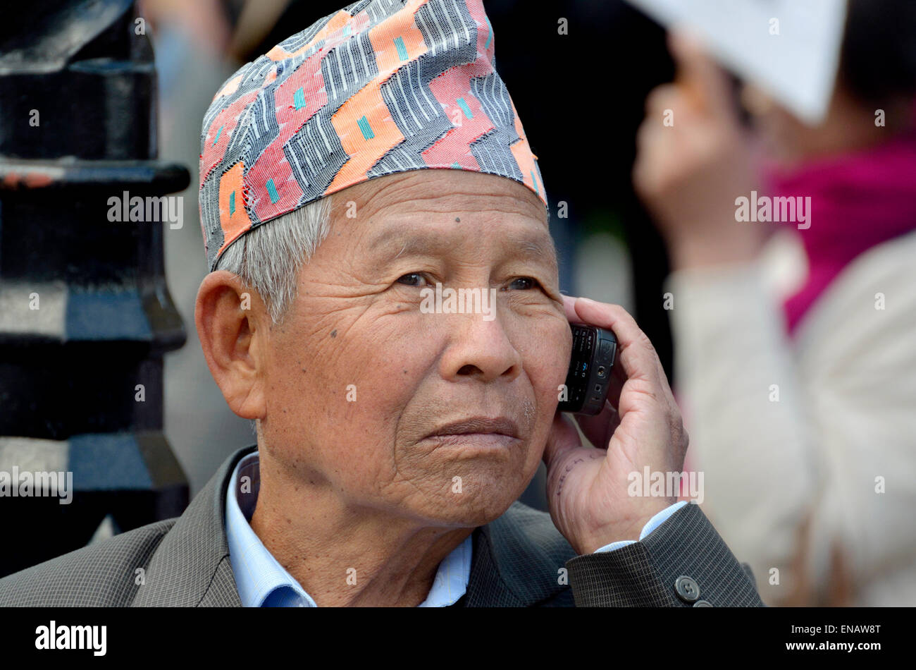 Elderly Nepalese man / retired Gurkha using his mobile phone, London 2015, wearing a Dhaka topi - traditional hat Stock Photo