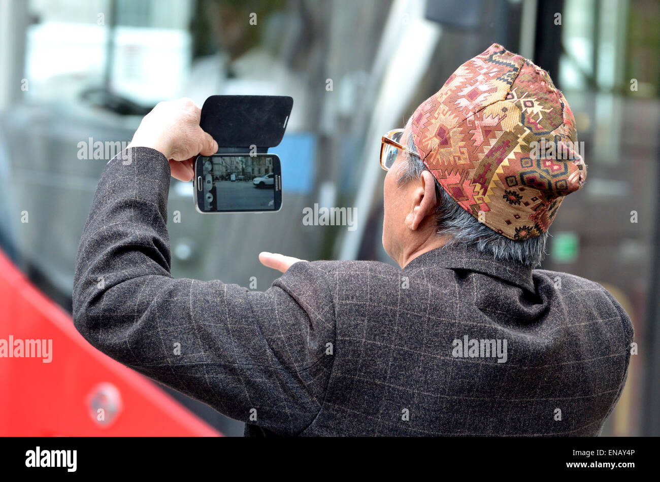 London, England, UK. Old Nepalese man (retired Gurkha) wearing a traditional Dhaka Topi (hat) taking a photo on his mobile phone Stock Photo