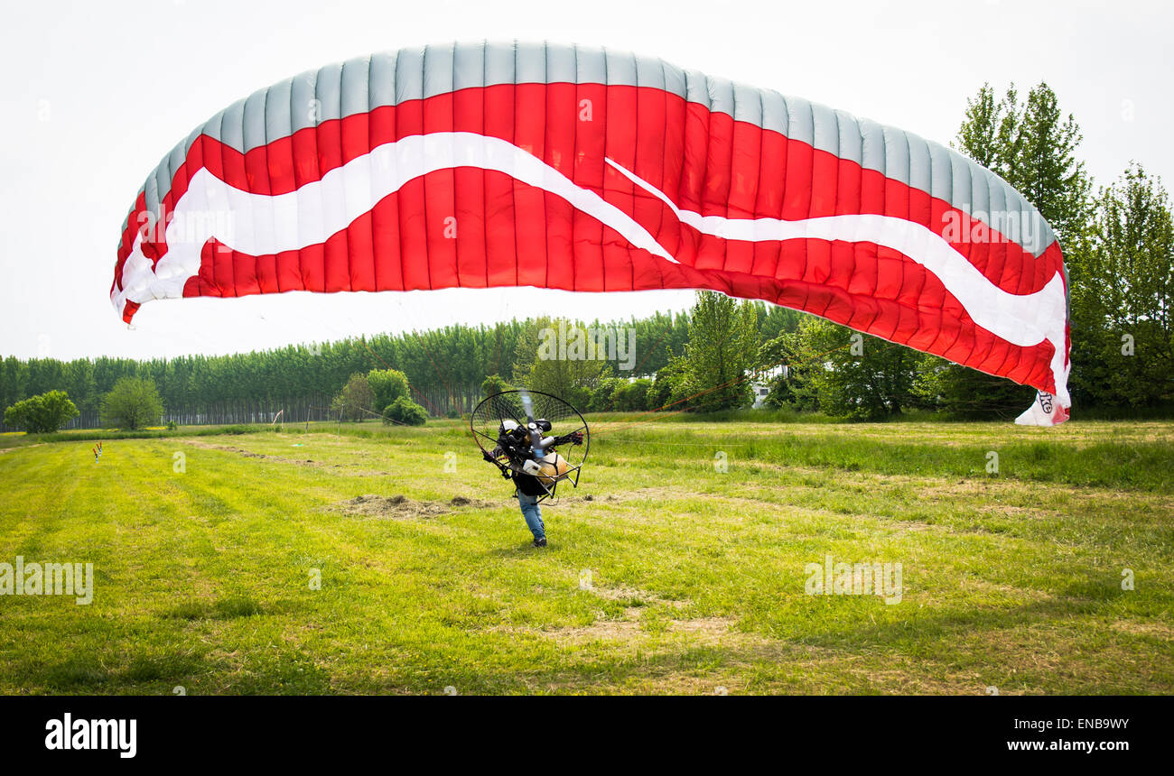 man with red motorized paraglider takes off from a green field Stock Photo