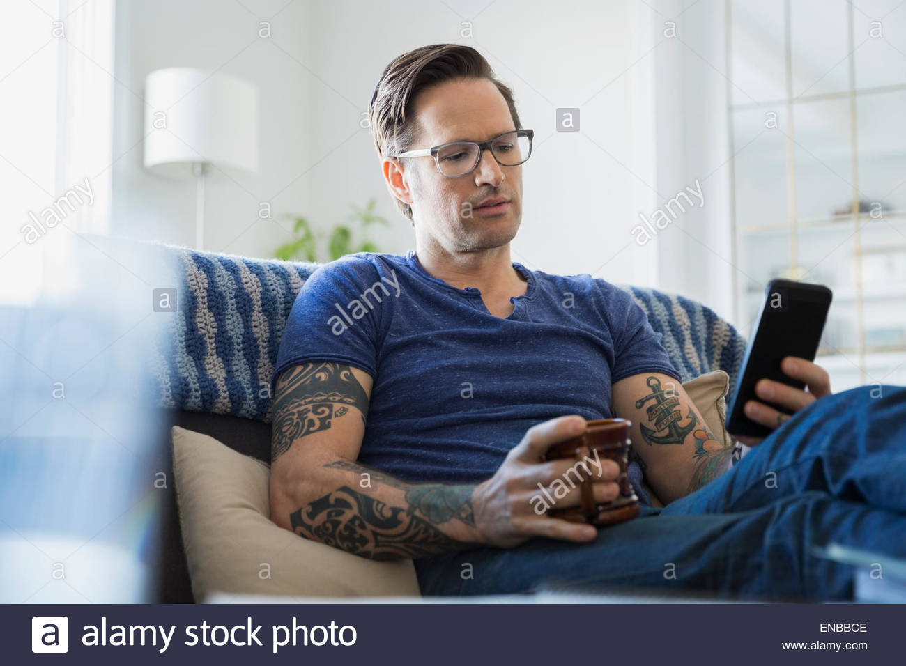 Man tattoos and coffee texting in living room Stock Photo