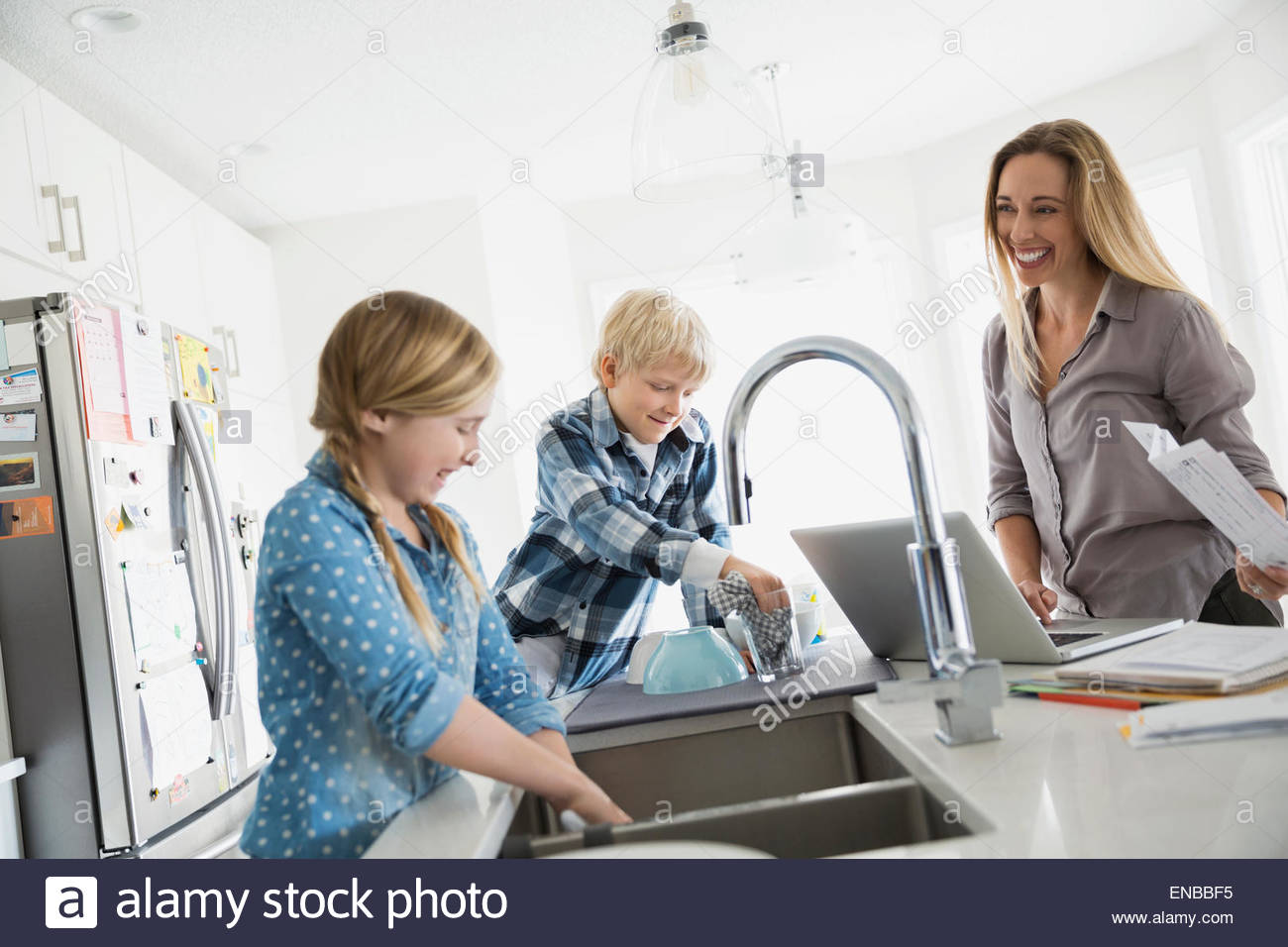 Mother at laptop watching children doing dishes Stock Photo