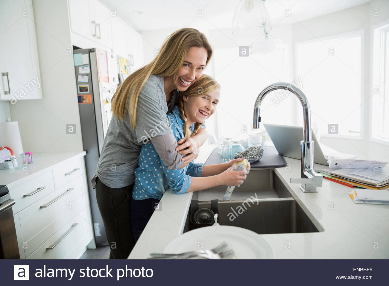 Portrait of smiling mother hugging daughter doing dishes Stock Photo