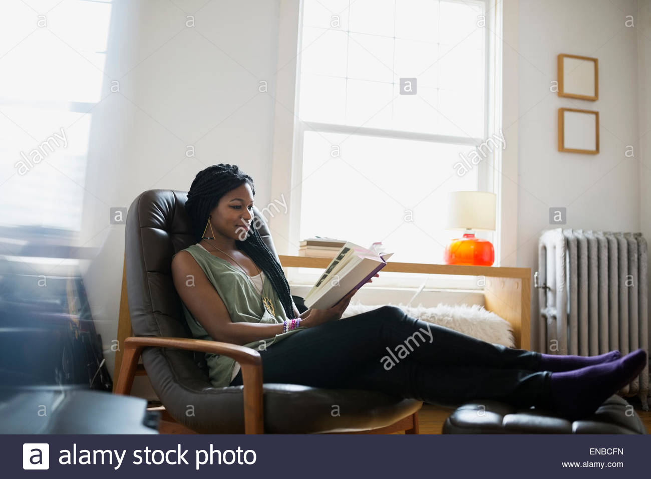 Woman reading book with feet up living room Stock Photo