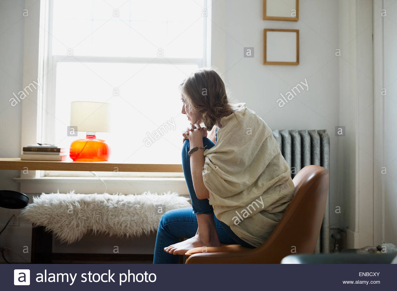 Pensive woman looking out living room window Stock Photo