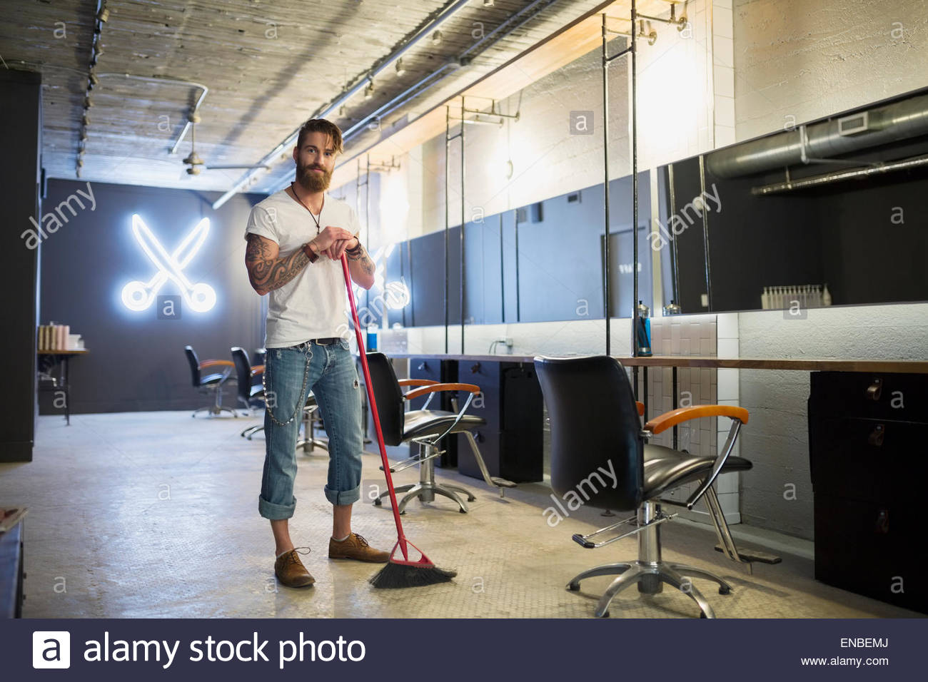 Portrait hipster hairstylist sweeping hair salon floor broom Stock Photo