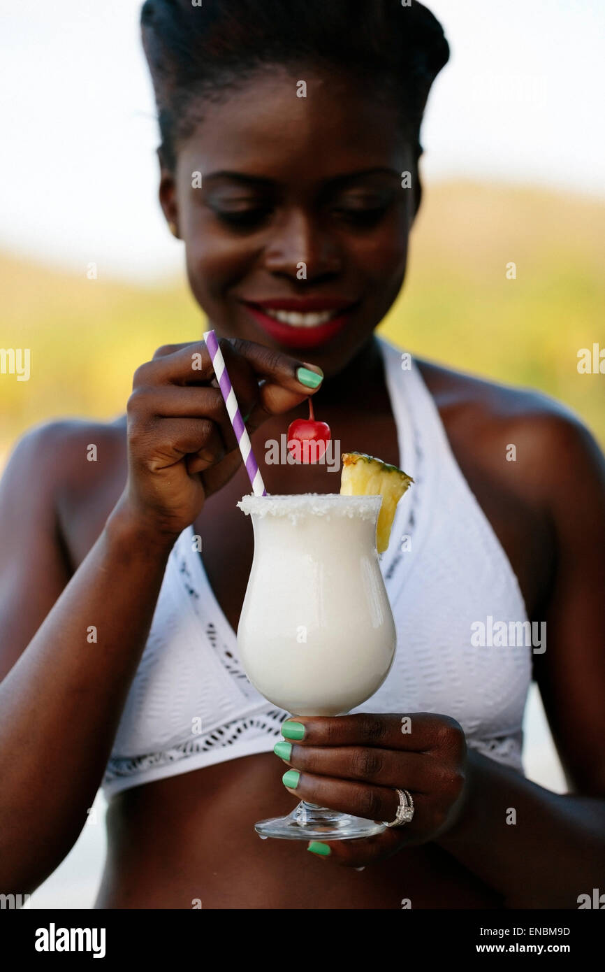 A glass of Pina Colada photographed in a Caribbean woman's hand on the beach. Stock Photo