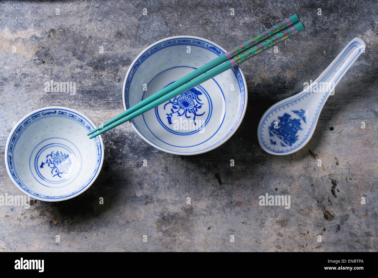Asian style porcelan bowls and turquoise chopstick over gray metal background. Top view Stock Photo