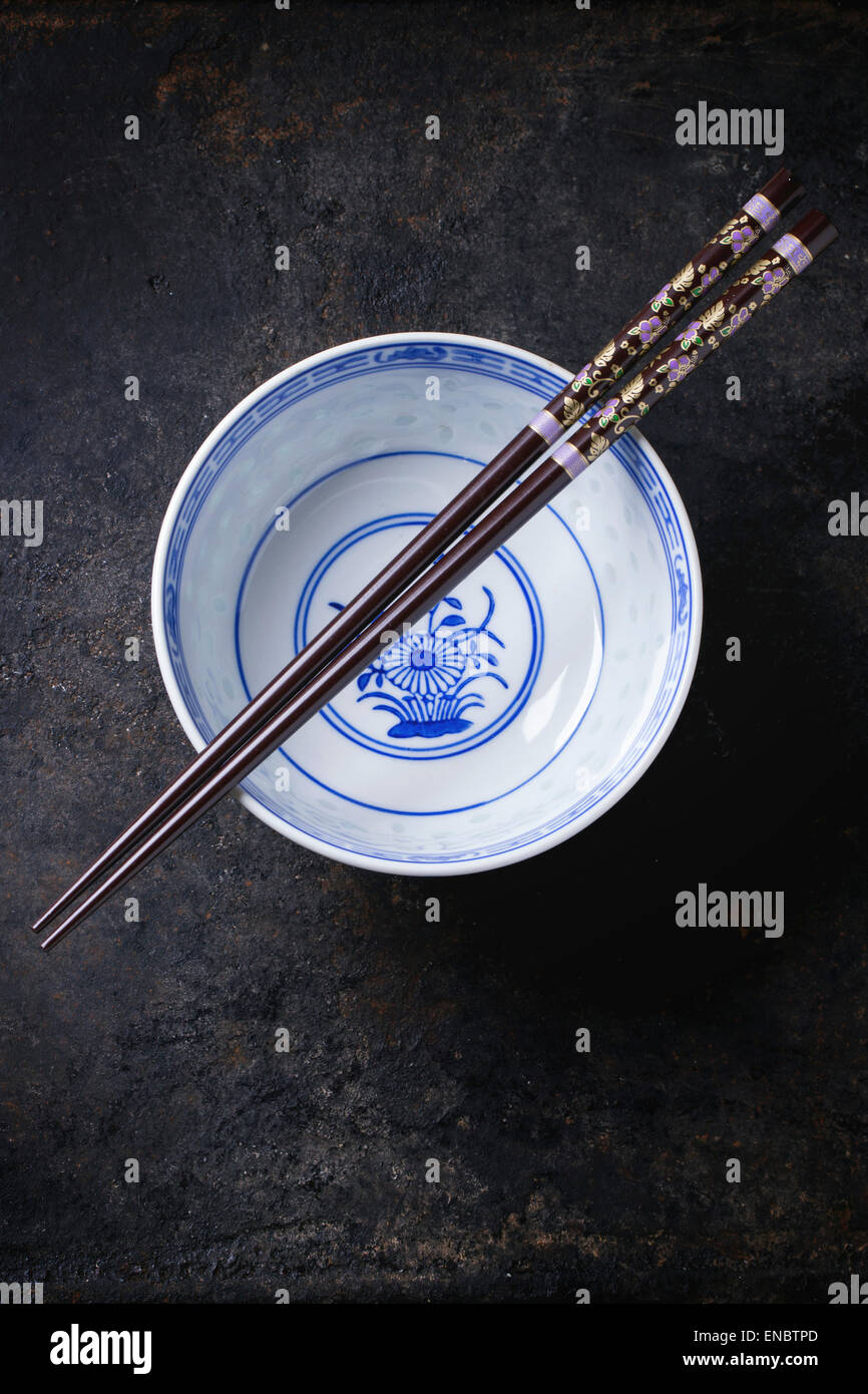 Asian style porcelan bowl and brown chopstick over black metal background. Top view Stock Photo