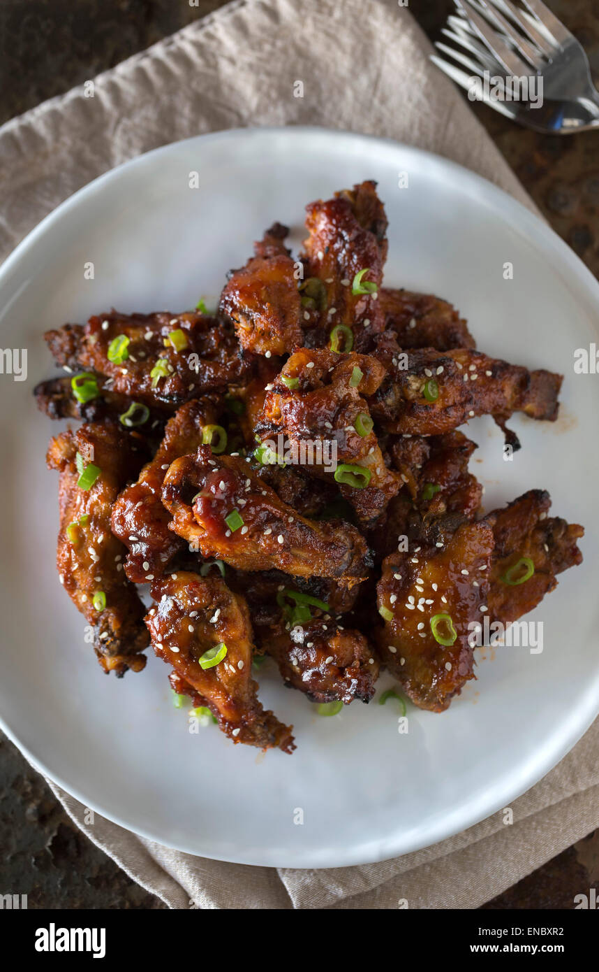 Asian-Style Sticky Chicken Wings sprinkled with sesame seeds and scallions served on a white plate. Stock Photo