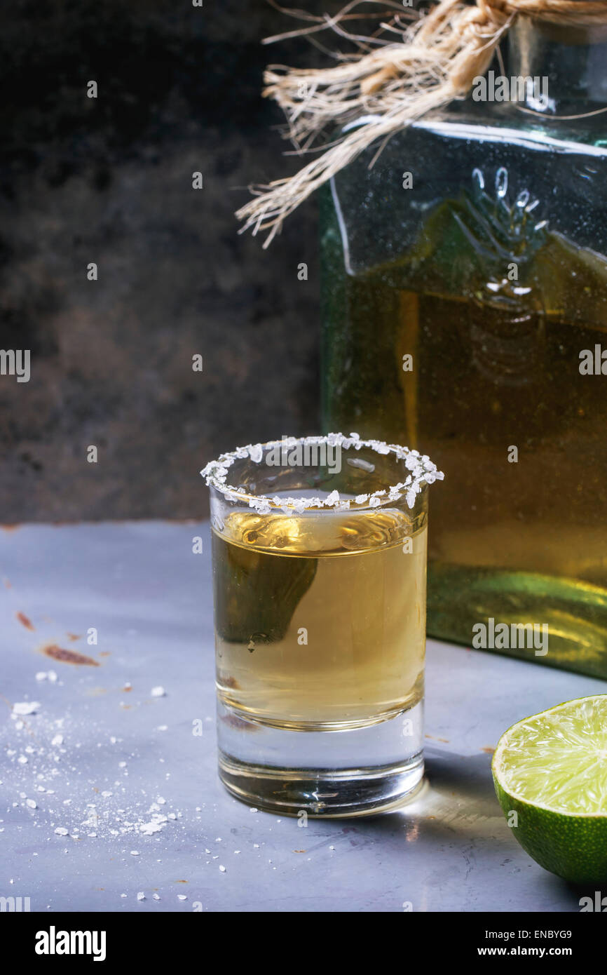 Short of tequila anejo with lime and salt over gray metal table Stock
