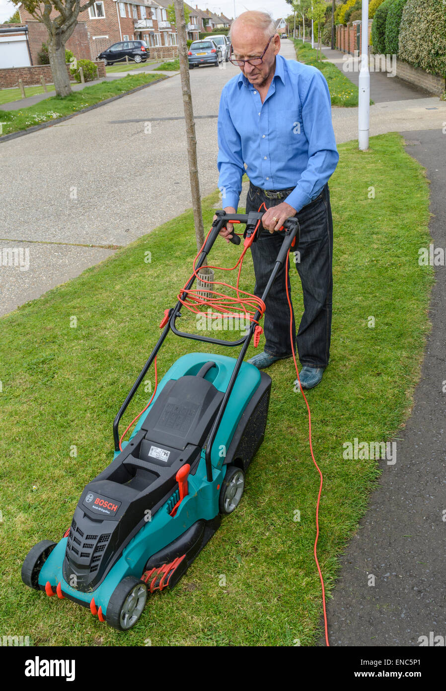 Elderly man mowing the grass verge by the roadside. Stock Photo