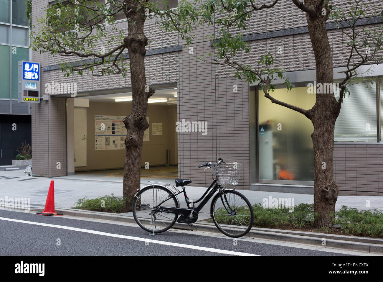 A lone bicycle parked on a side road between two trees and a red traffic cone, Tokyo, Japan. Stock Photo