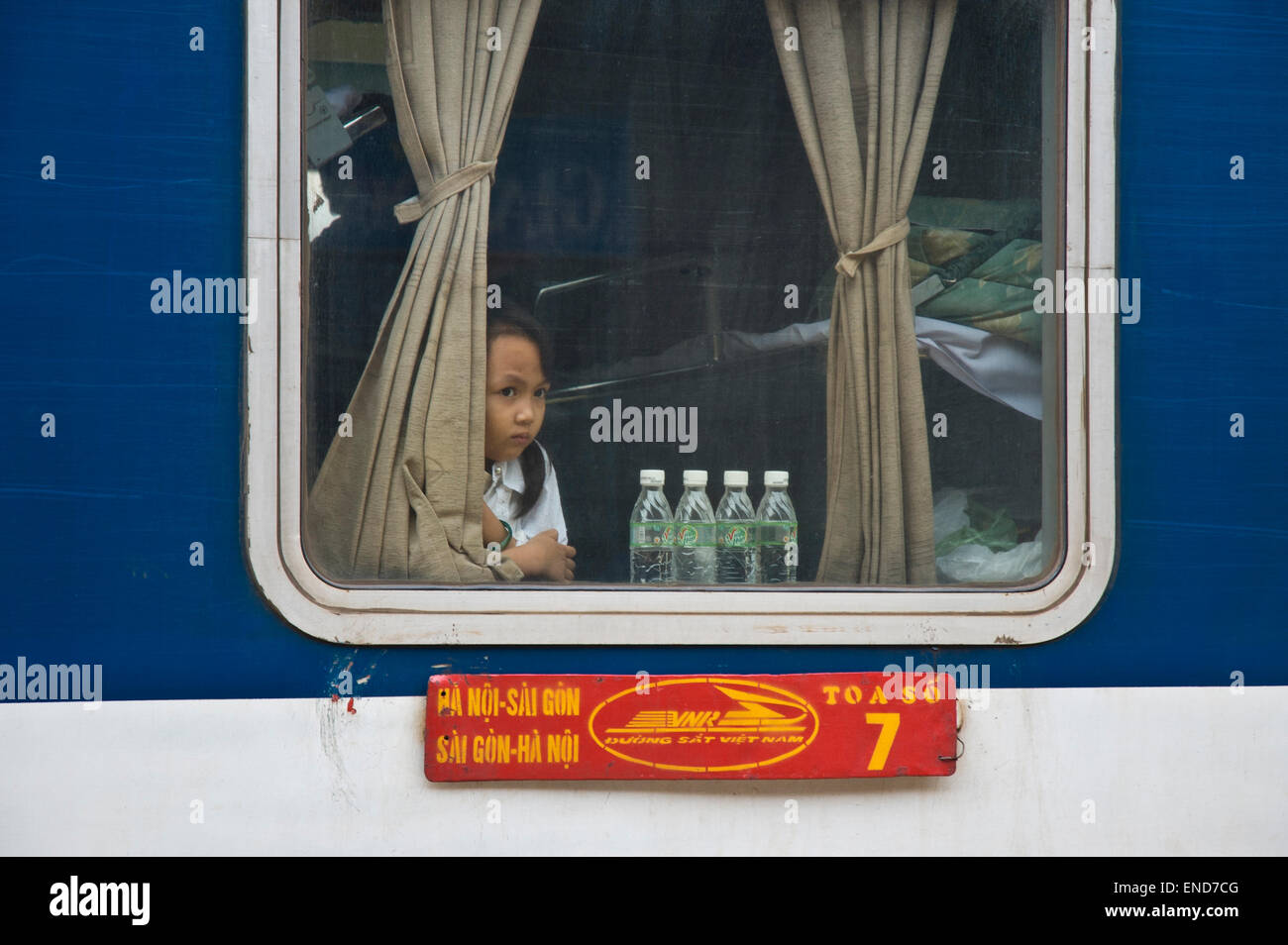 Girl looks out of a sleeper train window on the Reunification Express railway at a station between Hanoi and Saigon in Vietnam Stock Photo