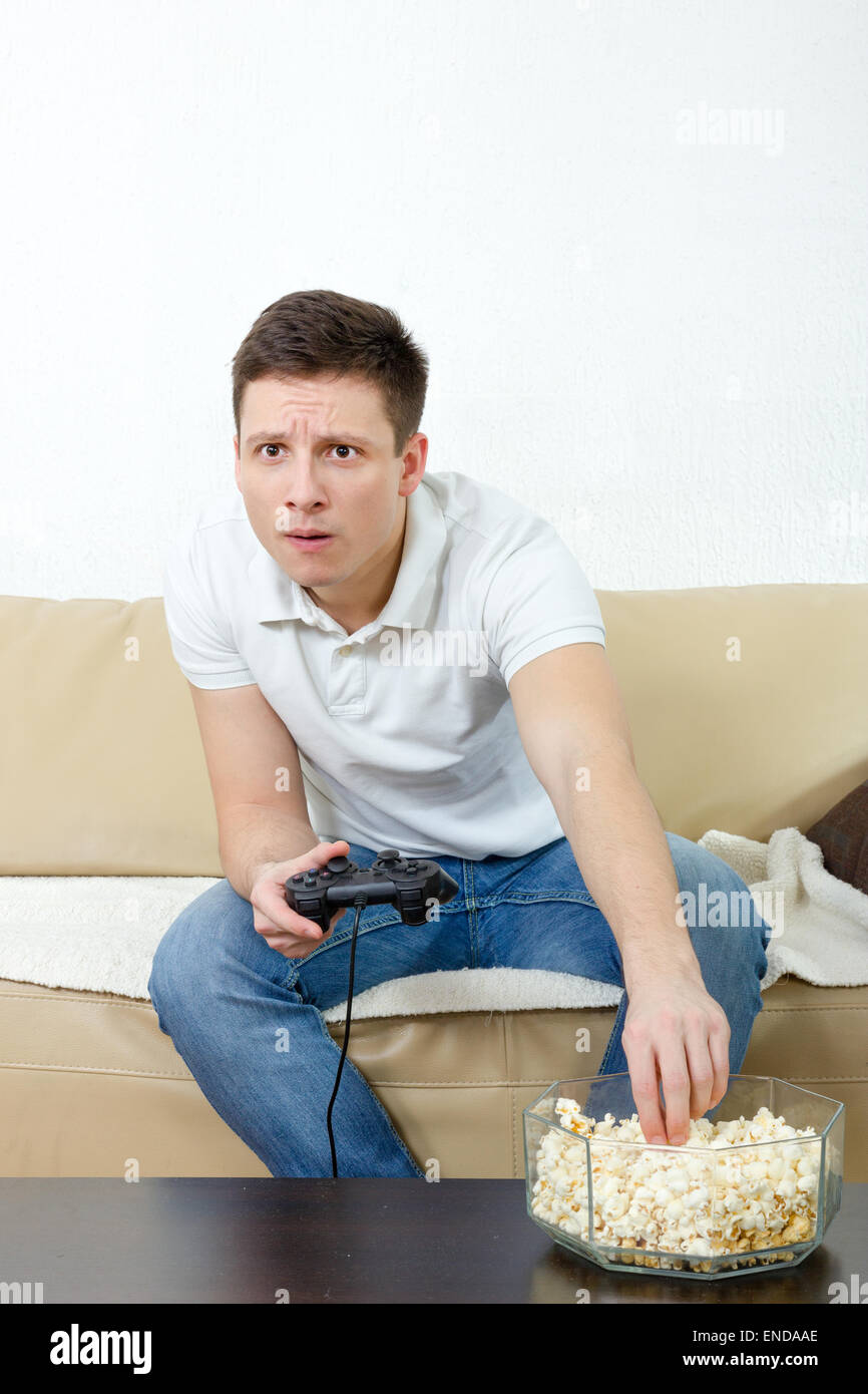 Focused man playing video game holding joystick and eating popcorn ...