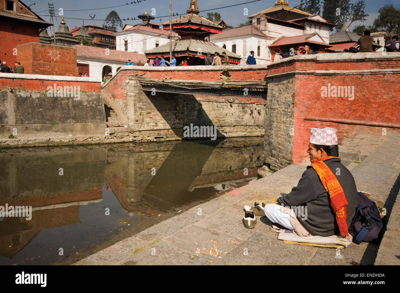NEPAL, Kathmandu, Pashupatinath, man in traditional dress sitting next to the Bagmati River (a tributary of the Ganges) with Pas Stock Photo
