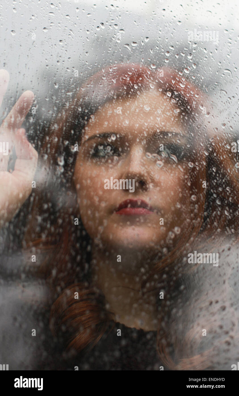 Pretty girl looking out of a window which is covered in rain drops Stock Photo