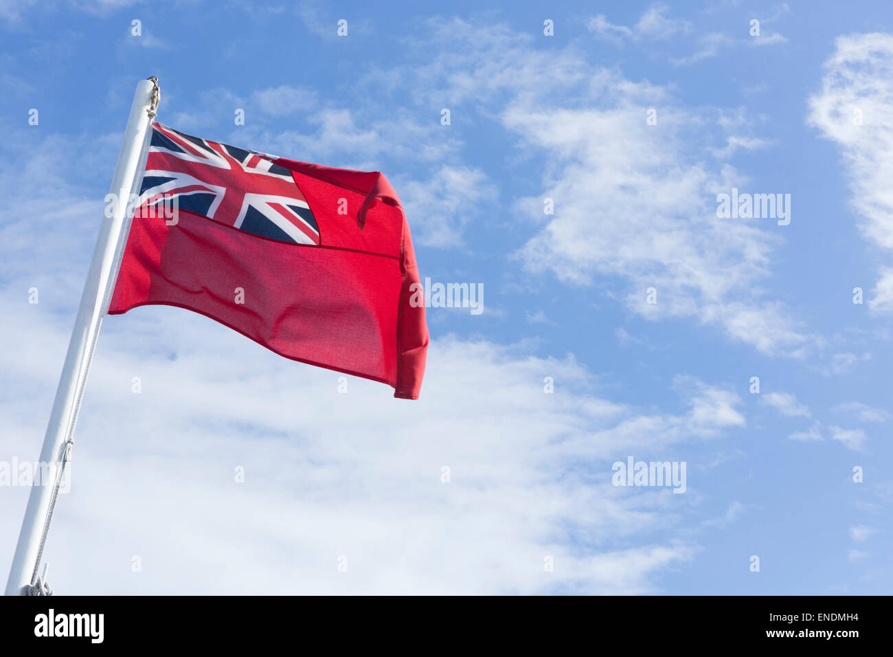 A Red Ensign Flag flying in a blue sky with white clouds Stock Photo