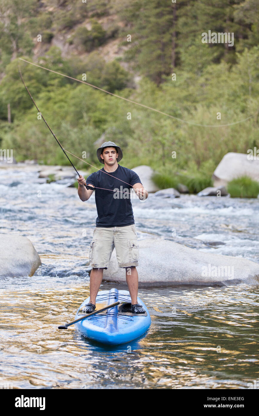 A young man flyfishing from a paddle board in a the rapids of the Feather River in Northern California. Stock Photo
