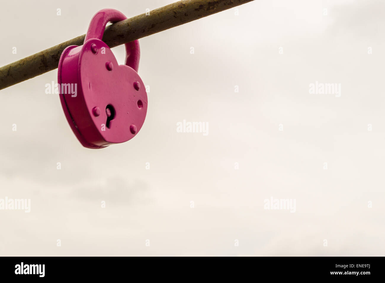 Locked pink painted padlock on an iron rod with visible keyhole Stock