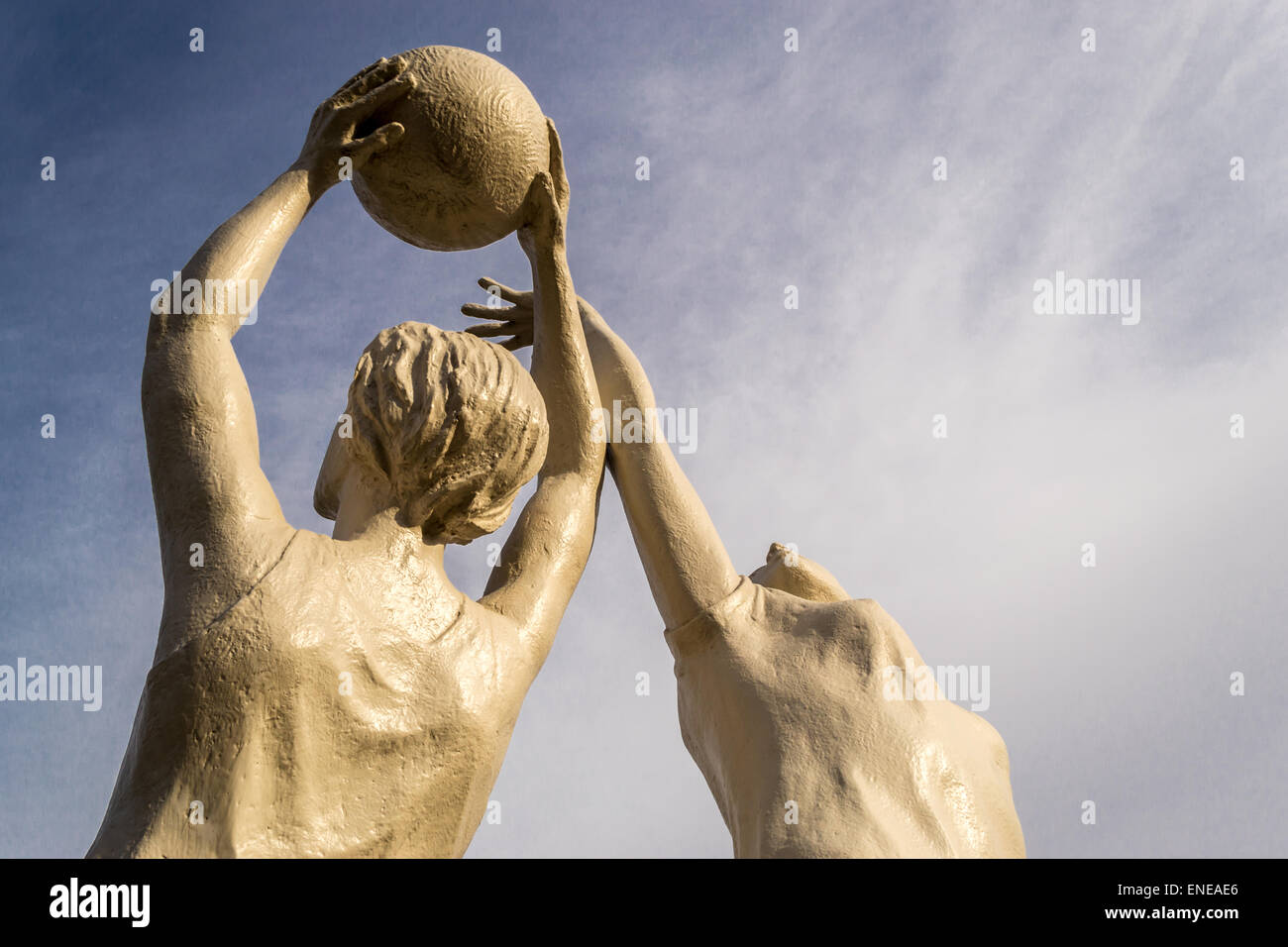 White stone statue of two women playing netball against a blue sky Stock Photo