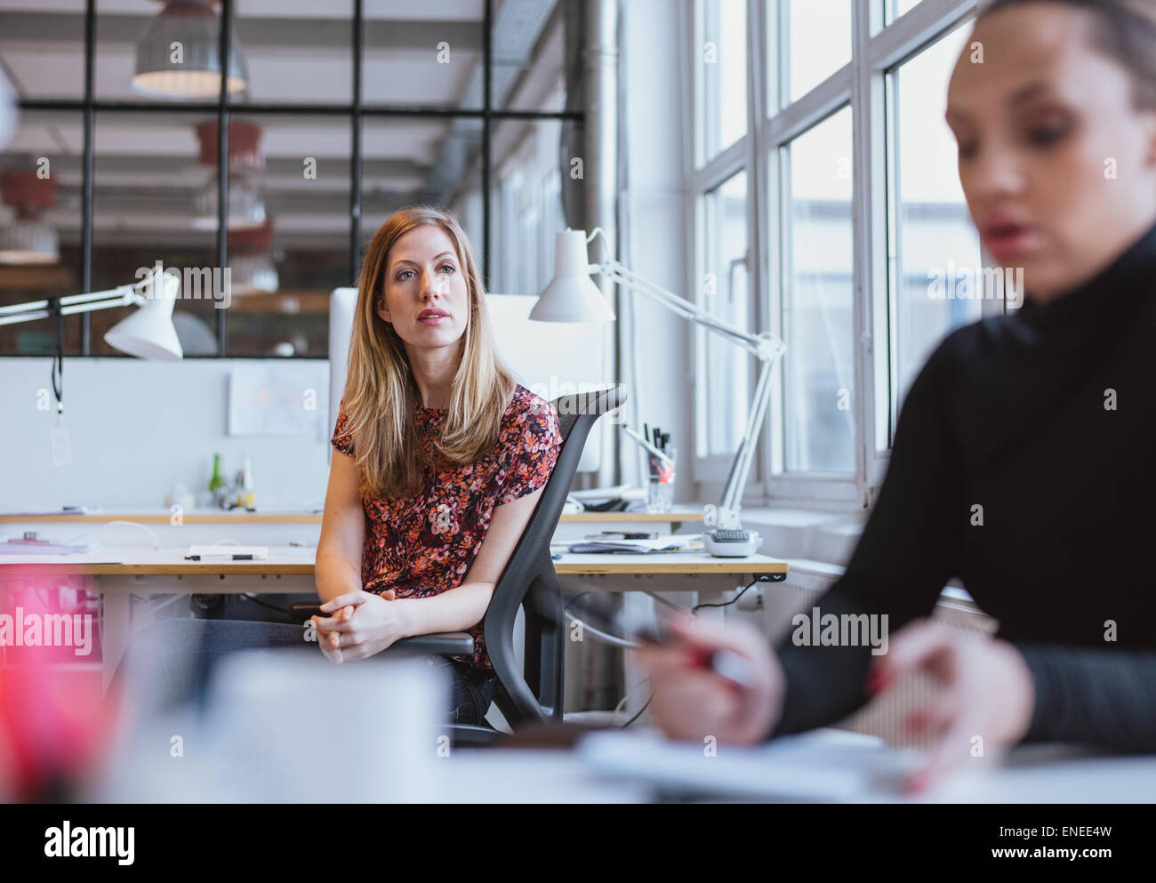 Image of young woman sitting at her desk looking away thinking. Female executive in office lost in thought. Stock Photo