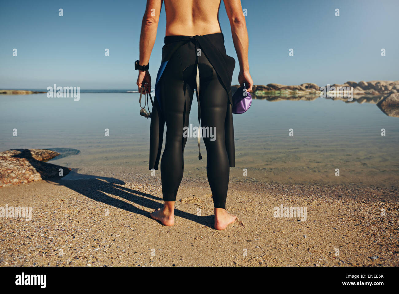Rear view of young man standing on lake wearing wetsuit. Cropped shot of a triathlete preparing for a race wearing a wetsuit pri Stock Photo