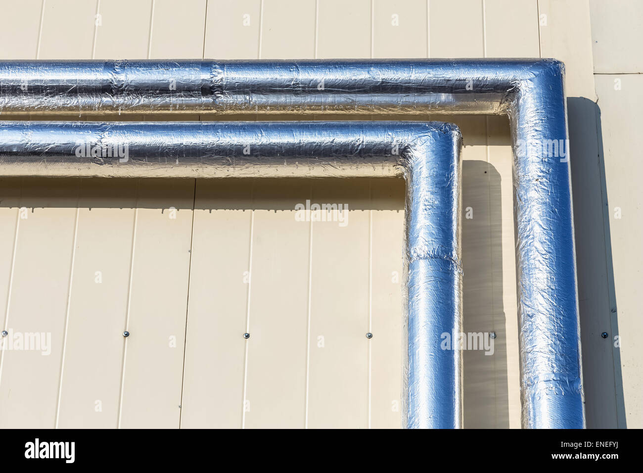 Metal chrome pipes on yellow plastic siding wall Stock Photo