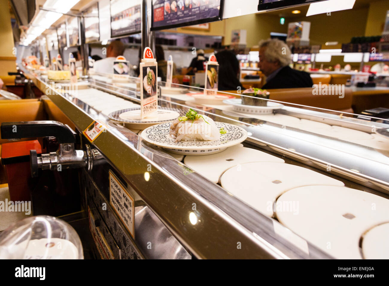 Interior of a typical Japanese conveyor belt sushi restaurant. Close up of various sushi and foods on plates moving along the conveyor belt. Stock Photo