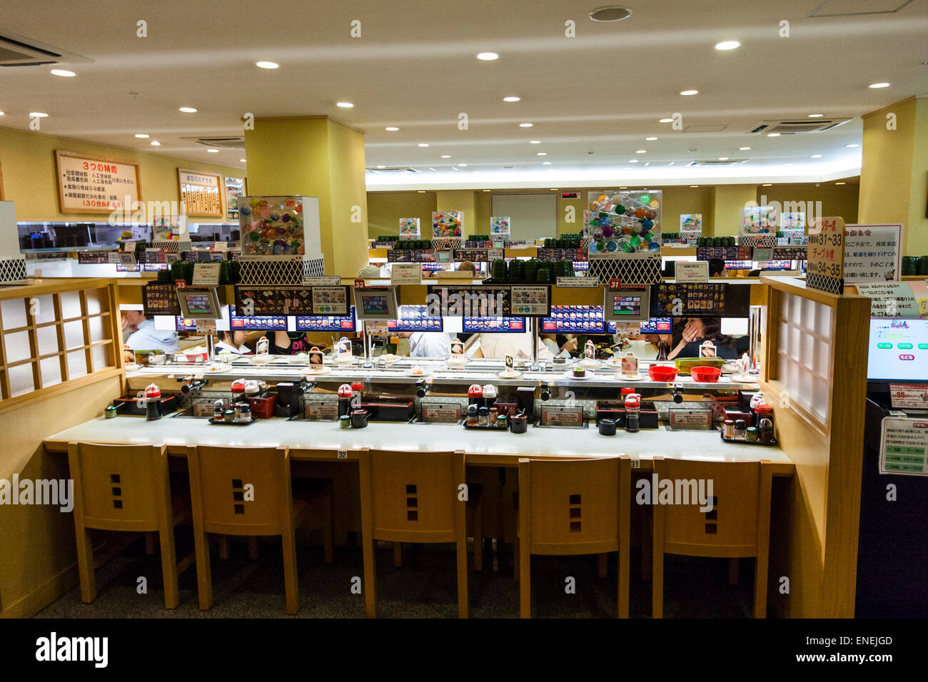 Interior of a typical Japanese conveyor belt sushi restaurant. Booth of five places against counter with condiments and conveyor belt behind. Stock Photo