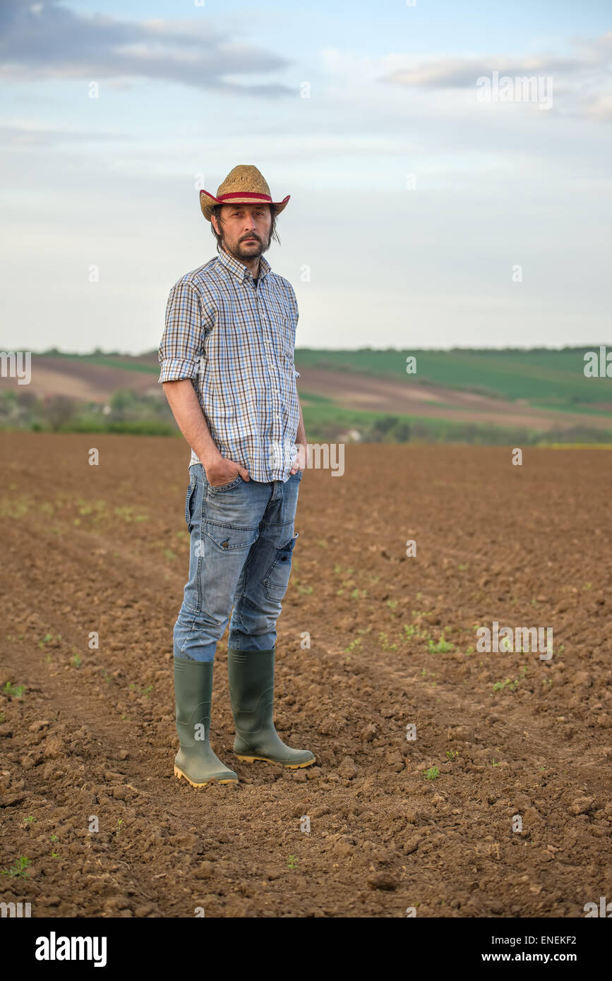 Portrait of Adult Male Farmer Standing on Fertile Agricultural Farm Land Soil, Looking into Camera Stock Photo