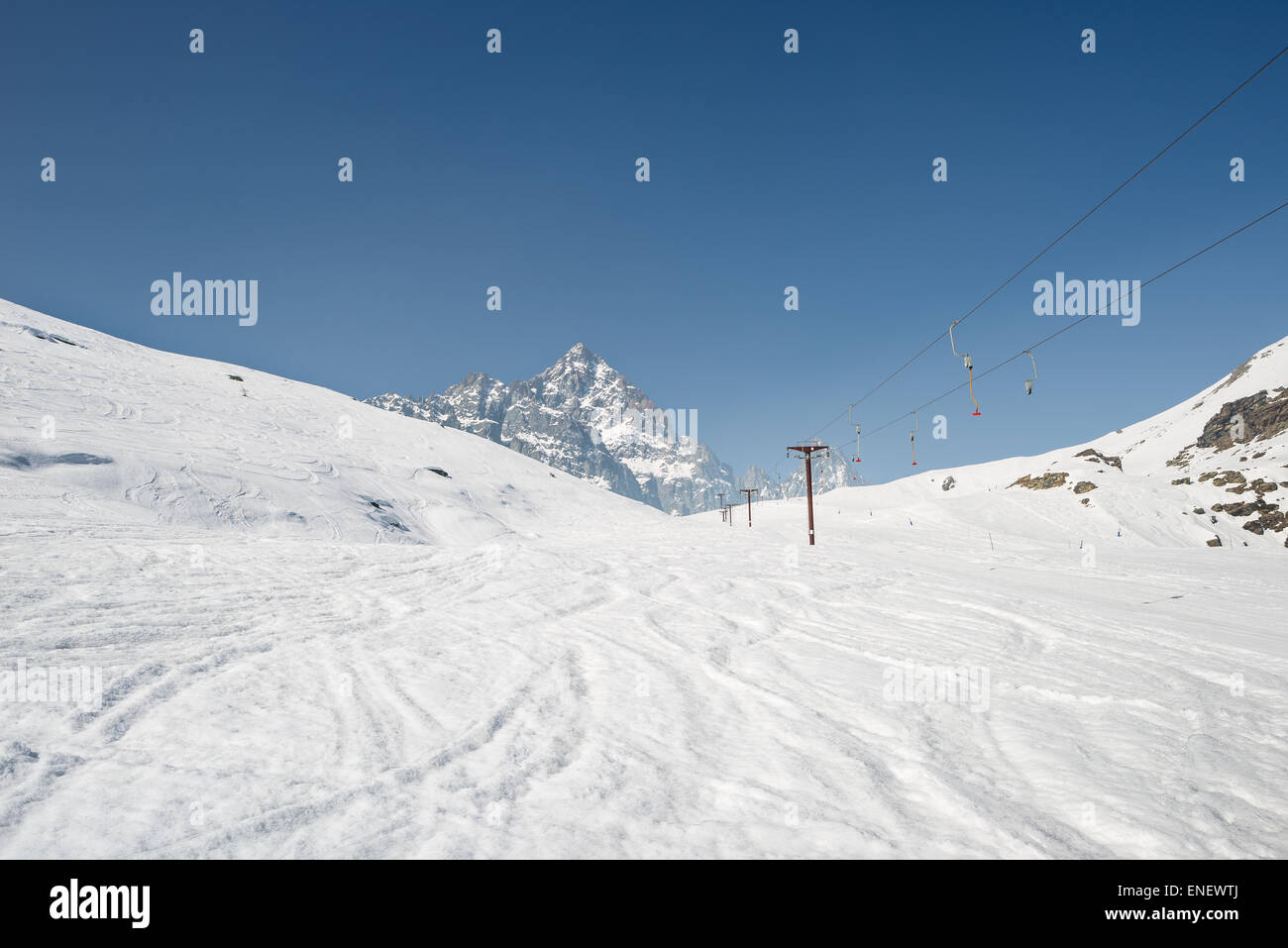 Ski resort with stunning view of high mountain peaks in the italian alpine arc, in a bright sunny day. Empty skilift. Stock Photo