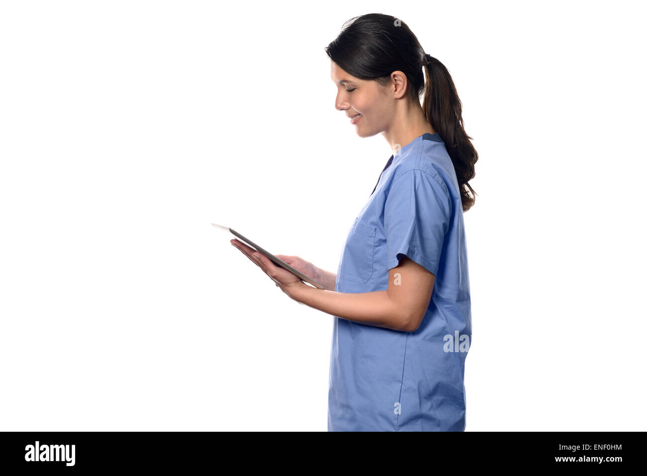 Happy young brunette nurse or doctor in blue uniform smiling while using a thin wireless PC tablet connected to internet, side p Stock Photo