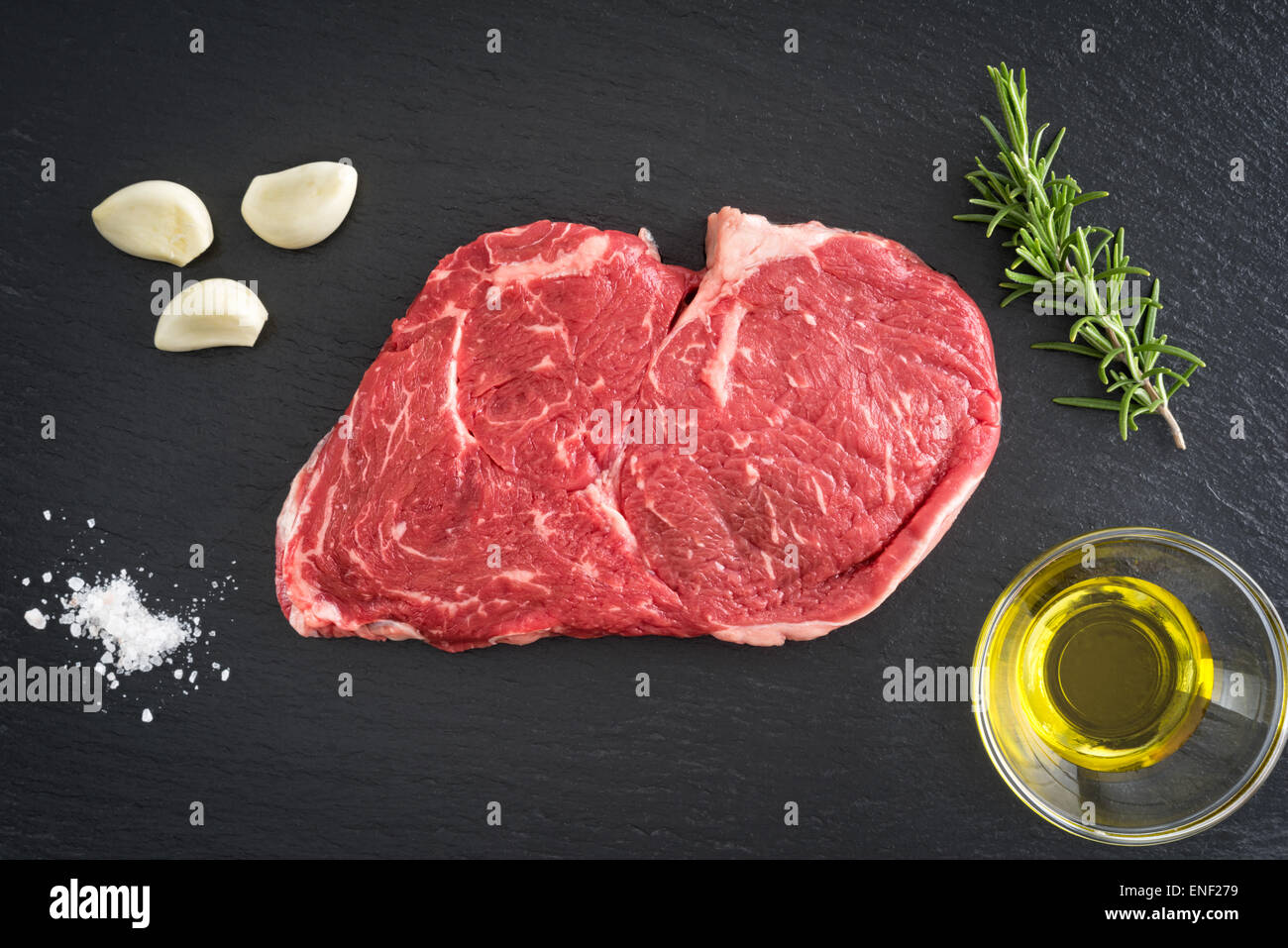 Fresh uncooked ribeye steak with garlic, salt, olive oil and rosemary