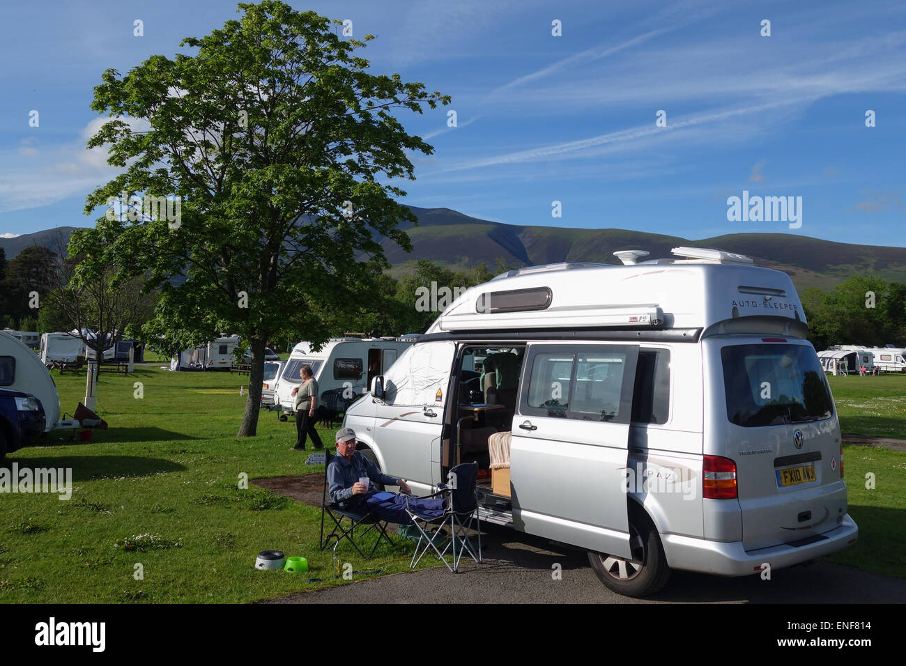 Man sitting outside a motorcaravan with feet up, Camping and Caravanning Club Site, Keswick, Lake District, Cumbria Stock Photo