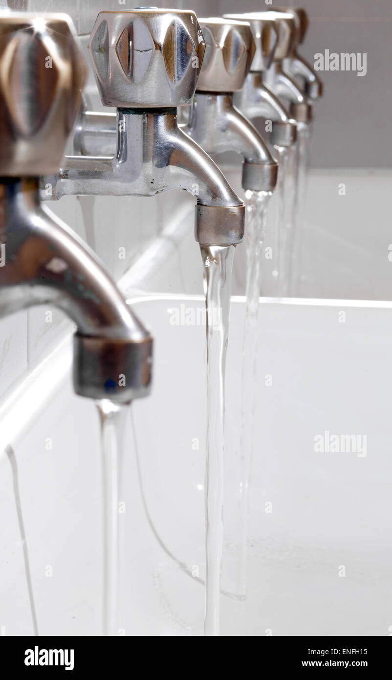 many steel taps with drinking water flowing in college bathroom Stock