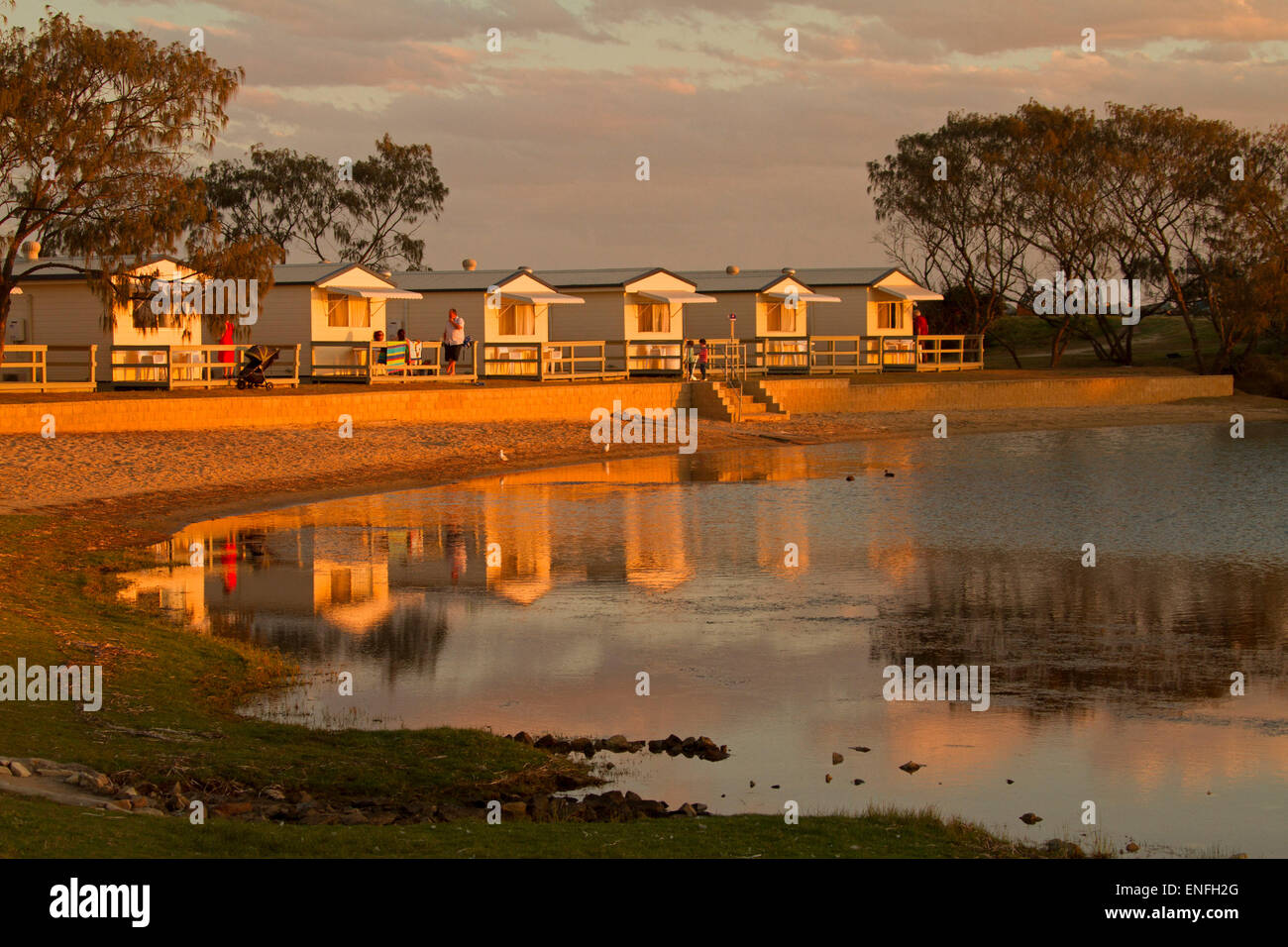 Waterfront holiday cabins by beach reflected in calm water of lake at sunset at Nambucca Heads NSW Australia Stock Photo
