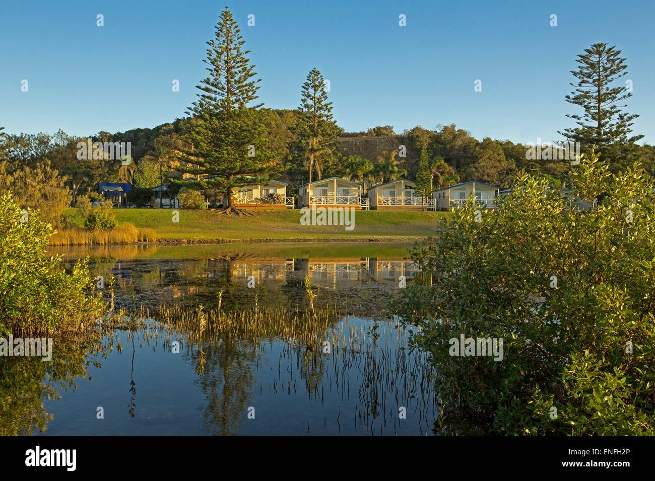 Waterfront holiday resort accommodation with blue sky and trees reflected in calm water of lake at Nambucca Heads NSW Australia Stock Photo