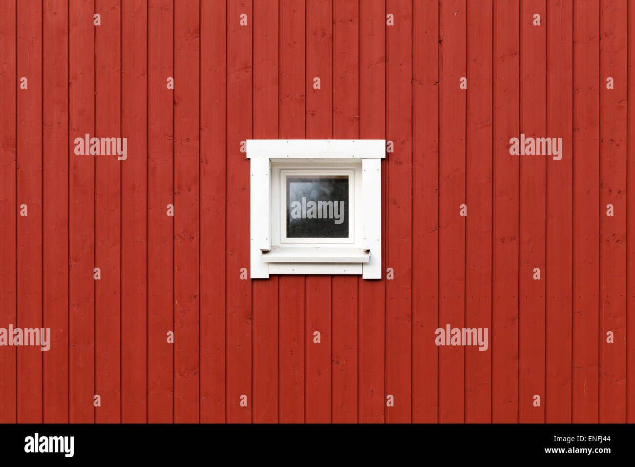 Red wooden wall with small window in white frame, typically Scandinavian living house architecture fragment Stock Photo