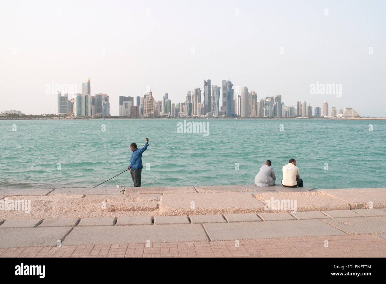 Three South Asian men passing time on the waterfront corniche in Doha, Qatar, with the city skyline seen in the background. Stock Photo