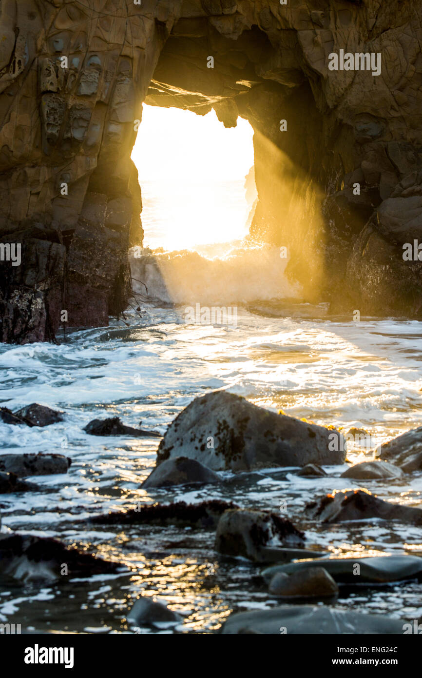 Sunbeam shining through rock formation to ocean waves Stock Photo