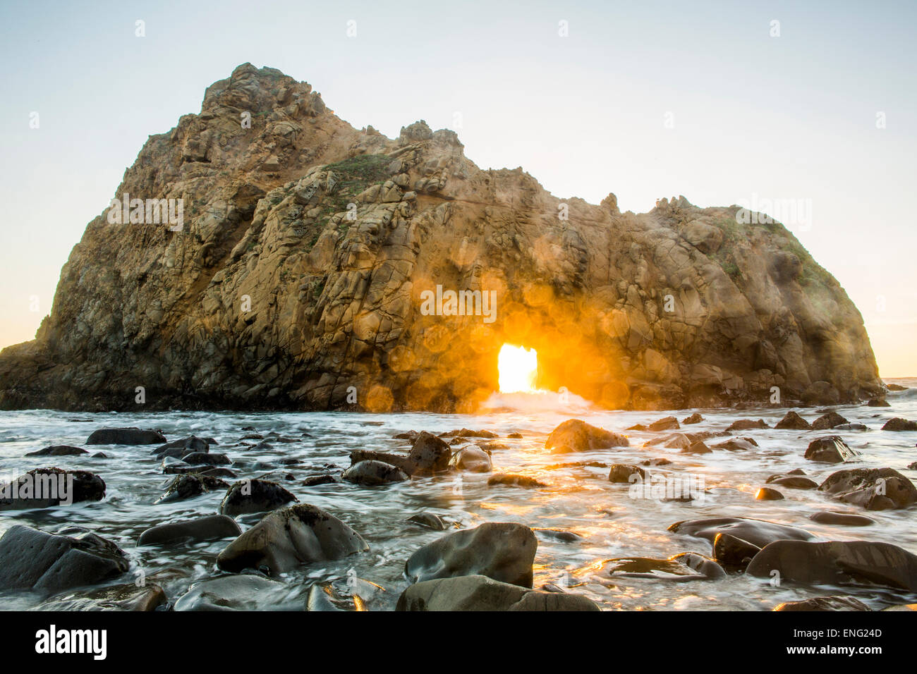 Sun shining through rock formation to ocean waves, Big Sur, California, United States Stock Photo
