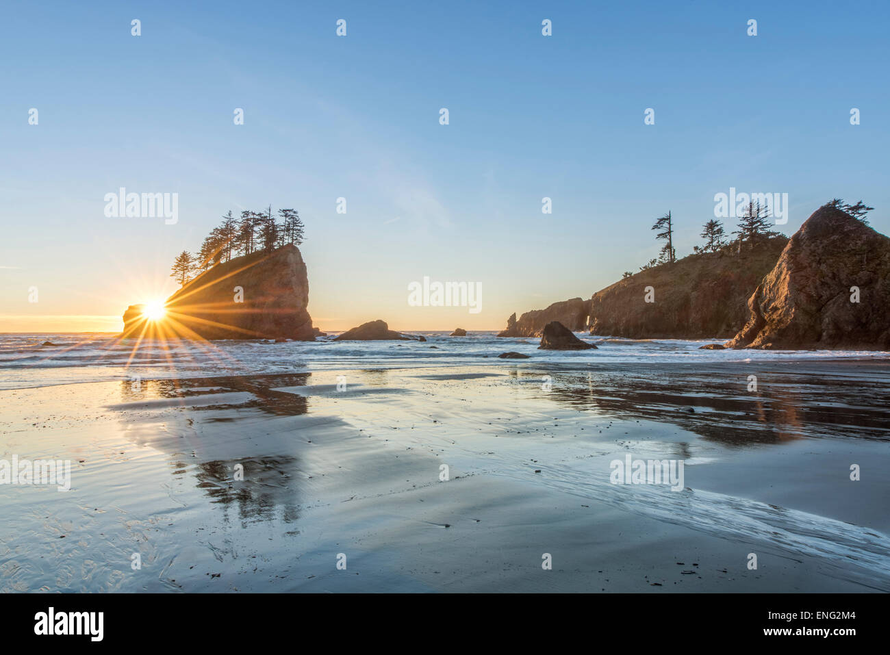 Sun rising over rock formations on beach Stock Photo